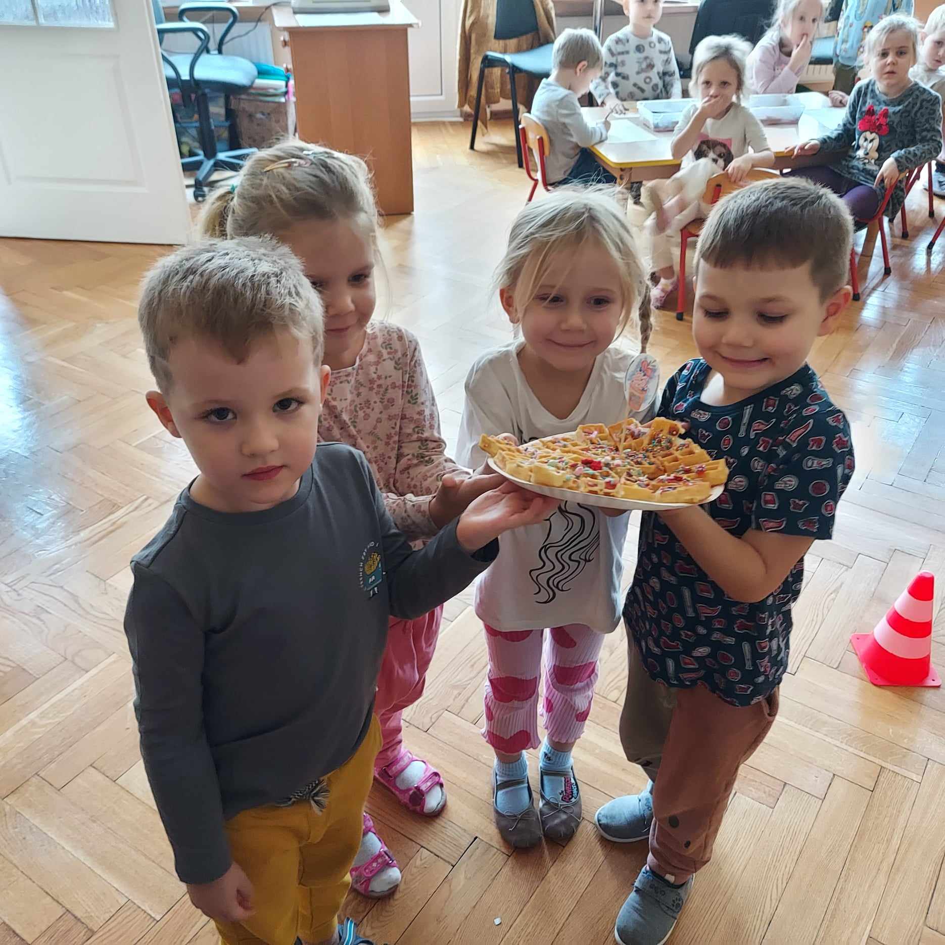 sala przedszkolna czworo dzieci prezentuje talerz z kolorowymi goframi