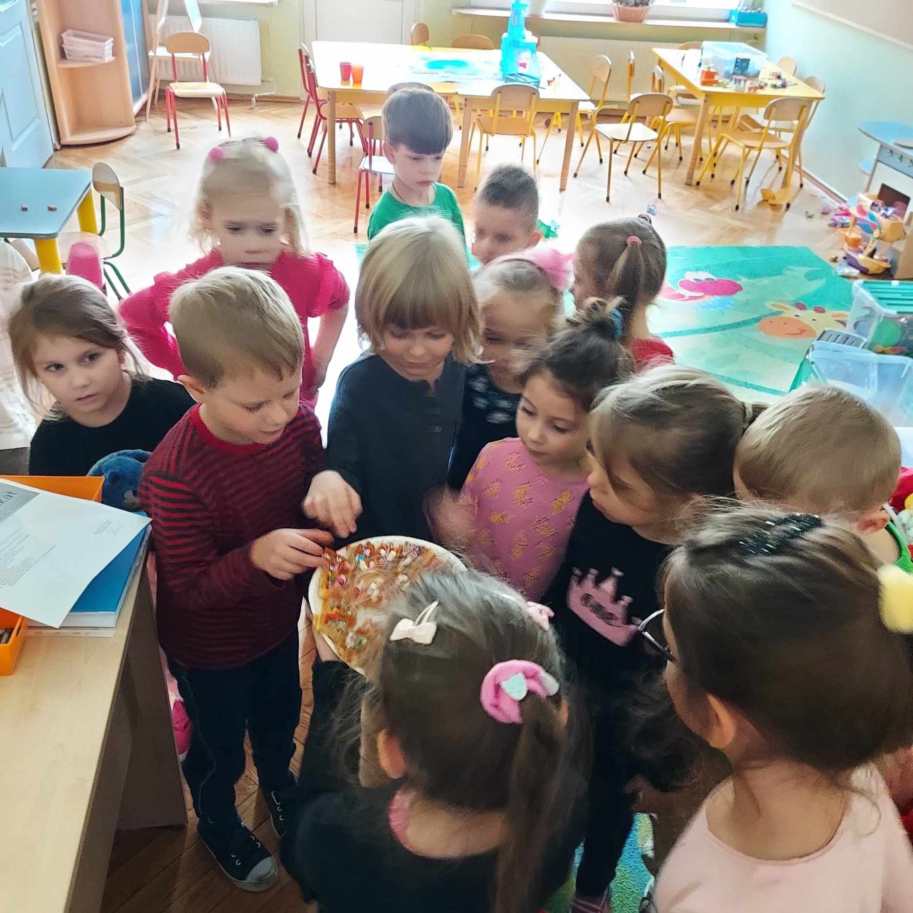sala przedszkolna dwie dziewczynki przekazują grupie dzieci talerz z kolorowymi goframi