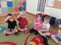 Grupa dzieci siedzi na dywanie i trzyma odblaskowe breloczki misie
