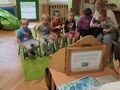 Grupa dzieci siedzi na krzesełkach nauczyciel opowiada bajkę z użyciem drewnianego teatrzyku