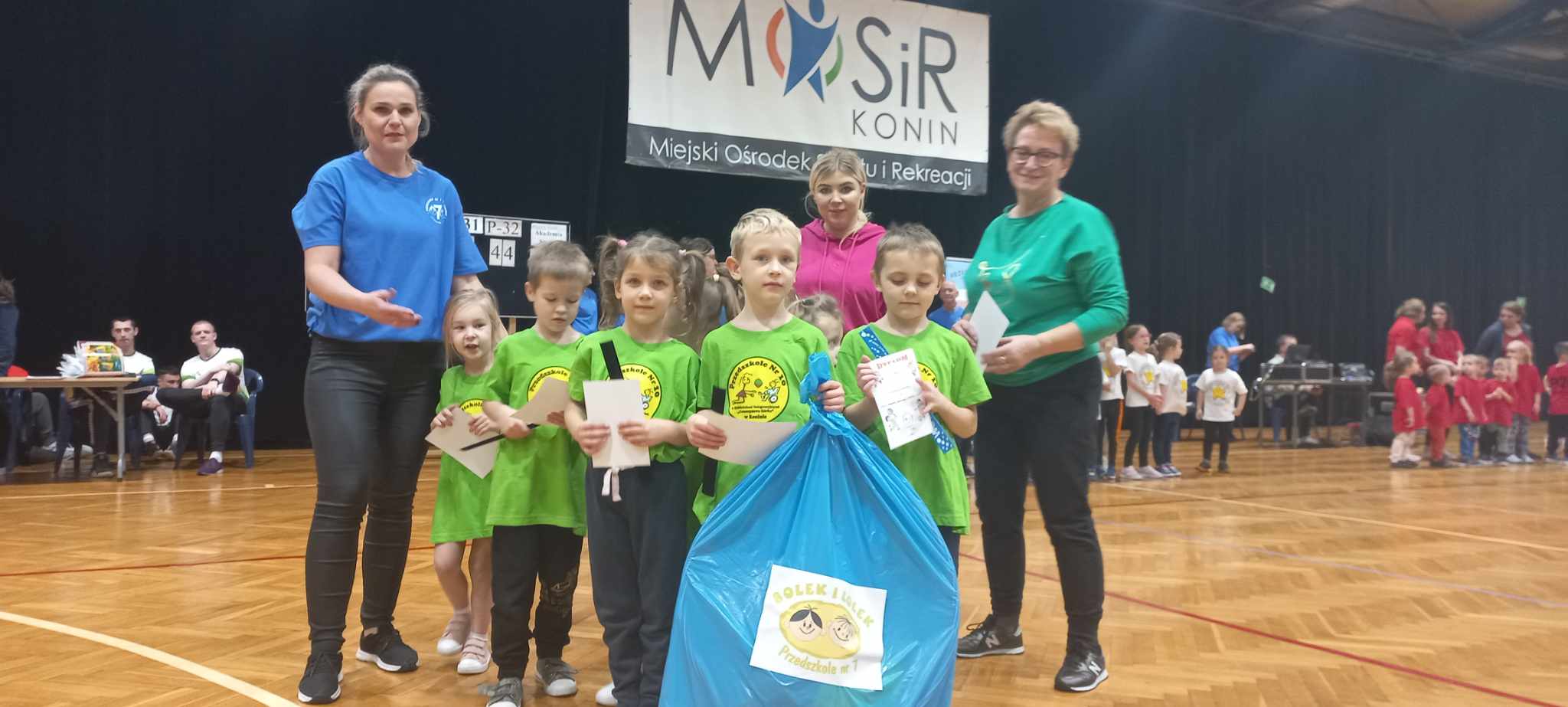 hala sportowa zdjęcie grupowe dzieci trzymają niebieski worek z logiem Olimpiady Bolka i Lolka