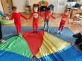 Dzieci ubrane na czerwono przekazują sobie hula hop na dywanie leży kolorowa chustą animacyjną.