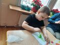 Dziecko przy stole odbija pomalowaną farbami choinkę na kartcejpg