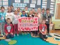 Grupa dzieci trzyma różowy plakat z napisem Dzień Przedszkolaka. 