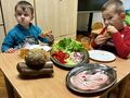 dwoje chłopców siedzi przy stoliku zjada rogale taca z warzywami leży przed nimi