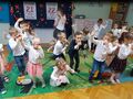 Grupa dzieci tańczy. Za nimi dekoracja z okazji Dnia Babci i Dziadka.
