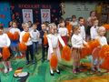 Grupa dzieci tańczy z pomarańczowymi pomponami. 