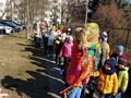 Grupa dzieci wraz z nauczycielami maszeruje chodnikiem i niesie Marzannę ze słomy