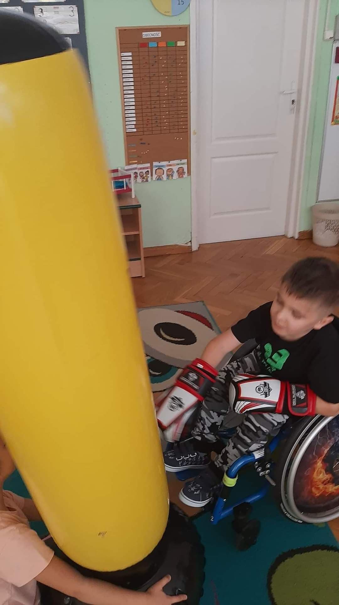 Chłopiec na wózku w rękawicach bokserskich uderza worek