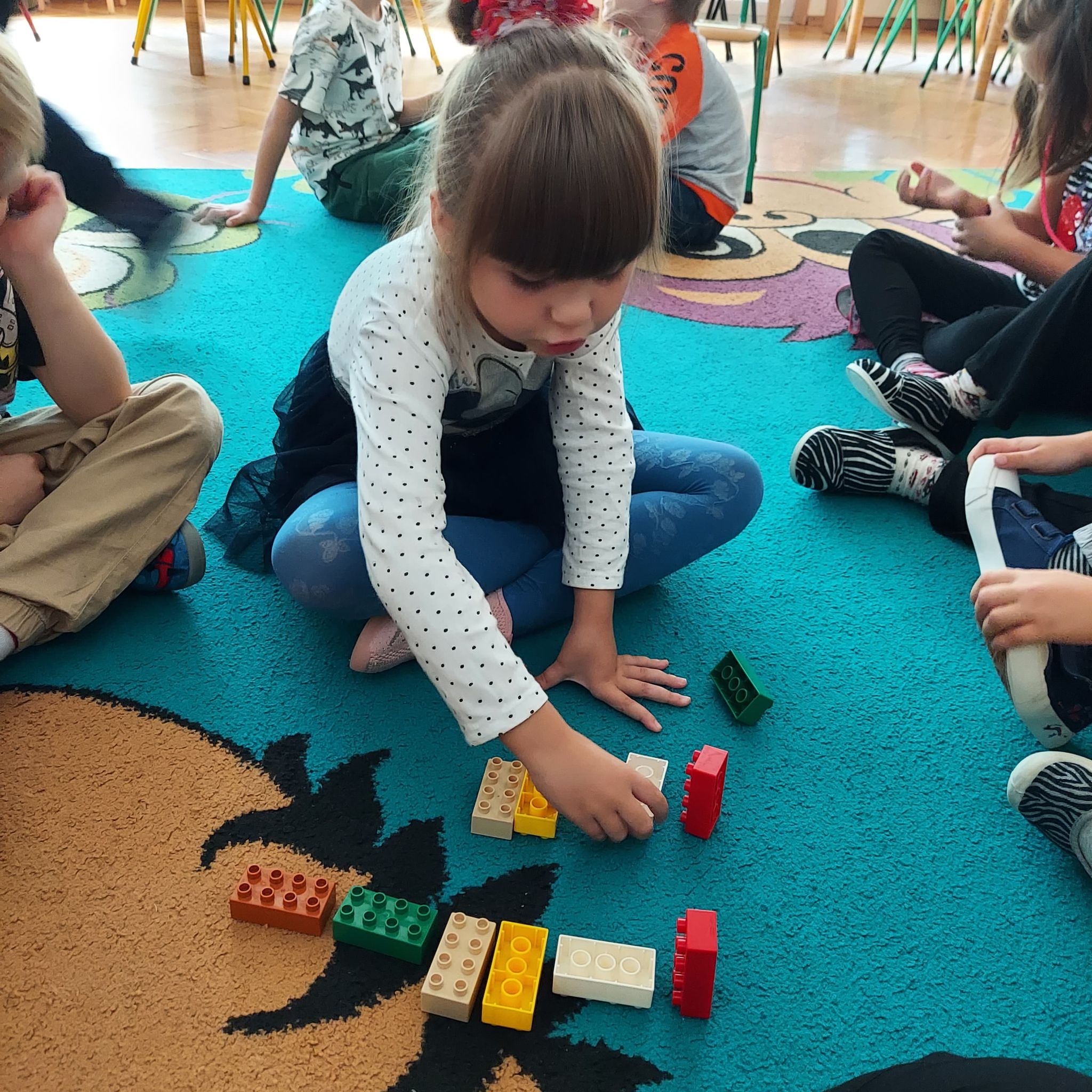 Dzieci na dywanie układają sekwencje z klocków