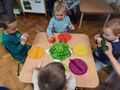 Dzieci siedzą przy stoliku, na którym są warzywa