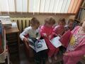 Grupa dzieci siedzi na małej kanapie i oglądają książki.