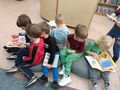 Grupa dzieci siedzi na pufach i ogląda książki. 