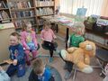 Grupa dzieci siedzi na pufach i ogląda książki. 