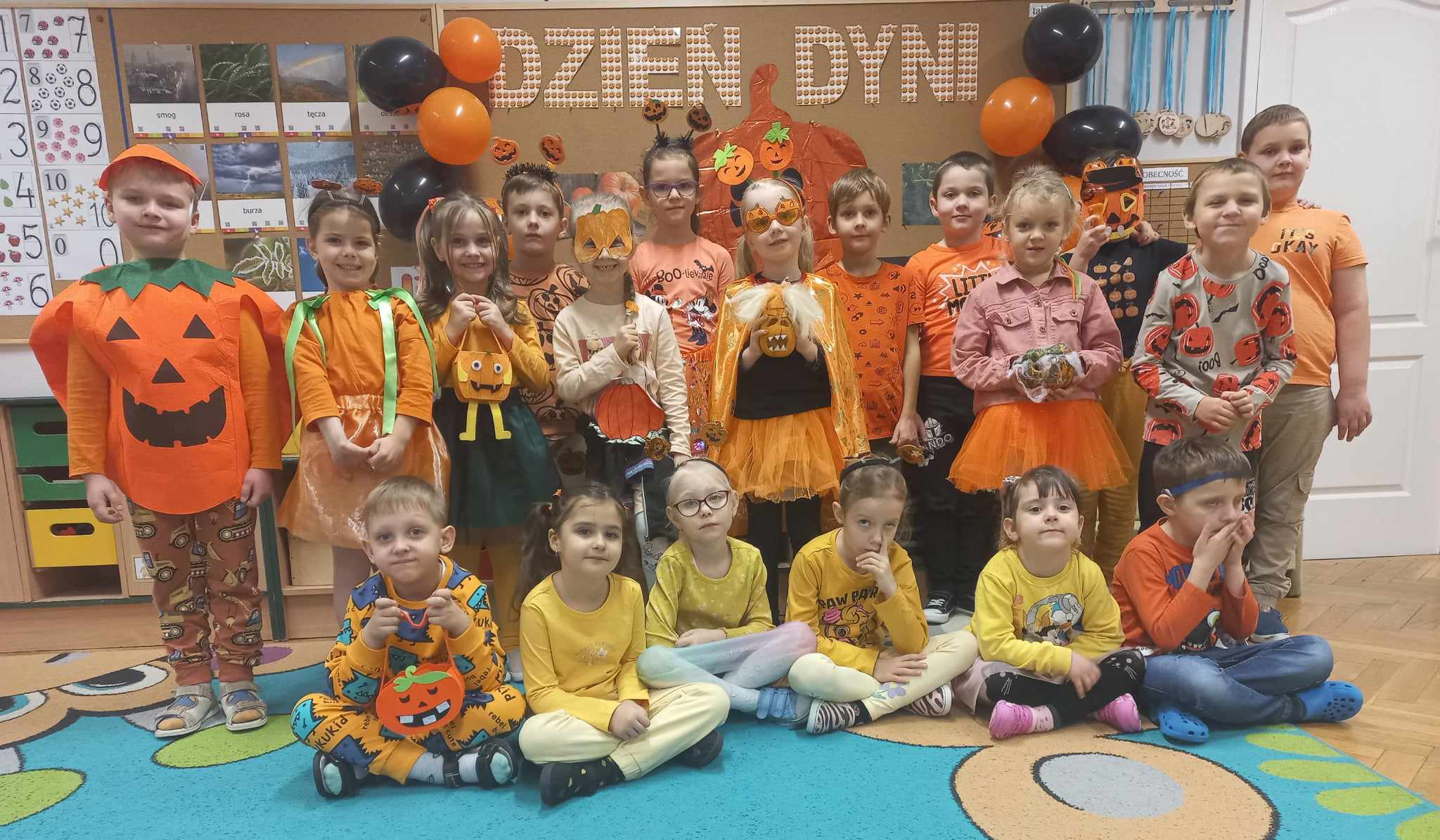 grupa dzieci ubrana na pomarańczowo na tle tablicy z napisem dzień dyni