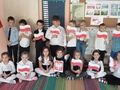 Grupa dzieci trzyma flagi Polski w rękach. Dziewczynka trzyma godło Polski