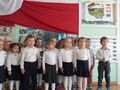 Grupa dzieci ubrana na galowo stoi przy fladze Polski