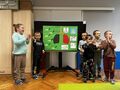 Grupa dzieci stoi przed ekranem, na którym wyświetlony jest zielony plakat palenie albo zdrowie
