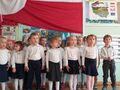 Dzieci ubrane na galowo stoją na baczność i śpiewają hymn