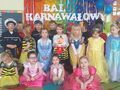 Grupa dzieci w strojach karnawałowych stoi na tle kolorowej ściany z napisem Bal karnawałowy