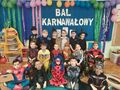 Grupa dzieci w strojach karnawałowych stoi na tle niebieskiej ściany ozdobionej balonami i napisem Bal karnawałowy