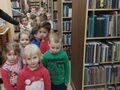 grupa dzieci idzie pomiędzy regałami z książkami