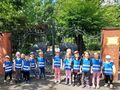 Grupa dzieci w niebieskich kamizelkach przed bramą parku.