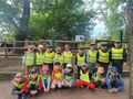 Grupa dzieci w żółtych kamizelkach w parku. Za nimi osiołek.