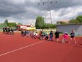 Grupa dzieci przeciąga linę że strażakami na boisku