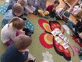 sala przedszkola dzieci siedzą na dywanie oglądają plansze
